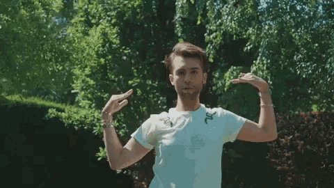 a man in a white t-shirt is flexing his arms in front of a forest .