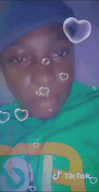 a boy wearing a blue hat and a green shirt has a tiktok sticker on his shirt