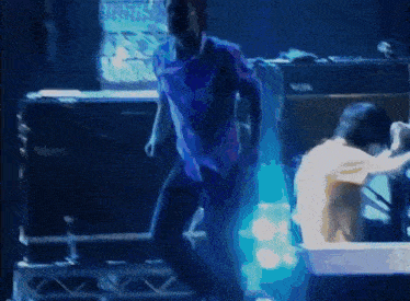 a man in a blue shirt is dancing on a stage in front of a vox amplifier .