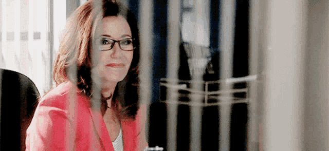 a woman wearing glasses and a red jacket is sitting in front of a glass door .