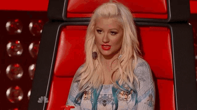 a woman with blonde hair and blue highlights is sitting in a red chair on a stage .