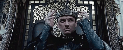 a man wearing a crown is sitting on a throne with his hands on his head
