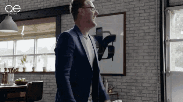 a man in a suit and glasses is standing in front of a brick wall and a sign that says ae