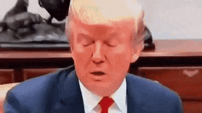 donald trump is sitting at a desk with his eyes closed .