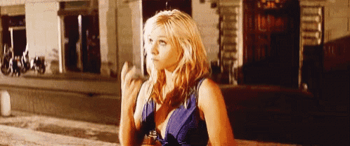 a blonde woman in a blue dress is sitting on a bench holding a bottle of beer .