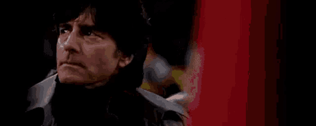 a man is sitting in a dark room with a red background and looking at something .