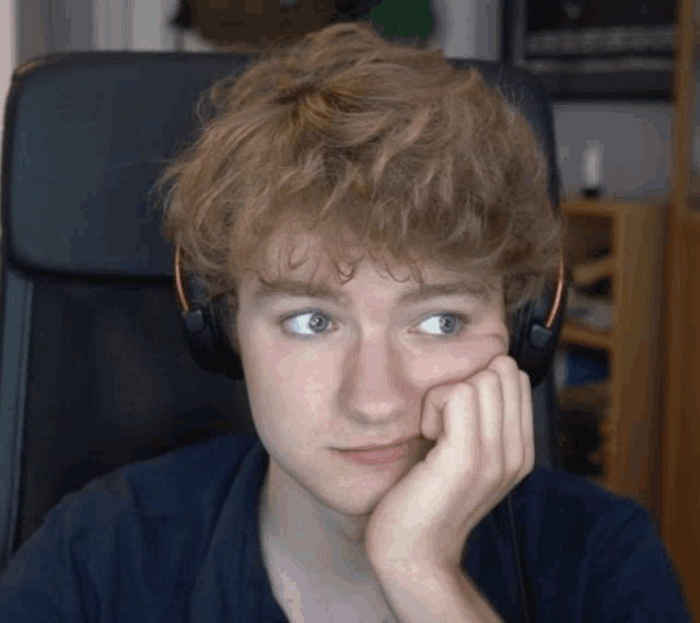 a young man wearing headphones is sitting in a chair with his hand on his chin