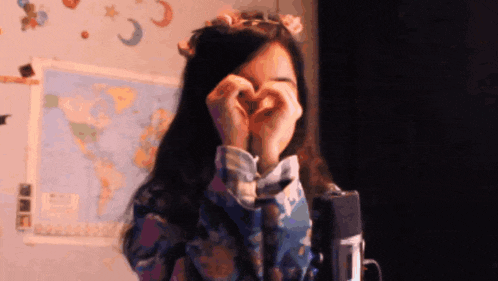 a woman is making a heart shape with her hands