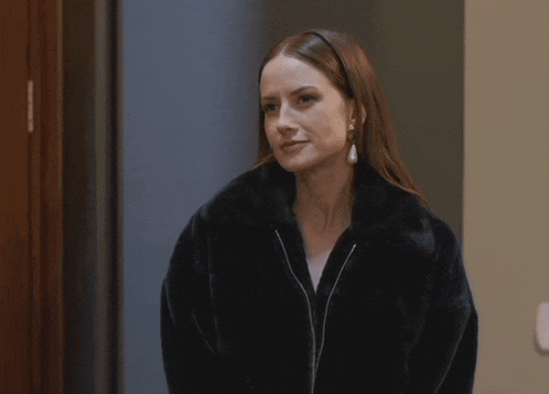 a woman in a black fur coat and pearl earrings