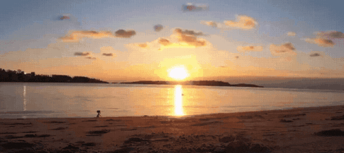 a sunset over a body of water with a person walking on the beach in the foreground