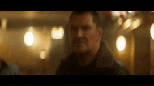 a man in a black jacket is standing in a dark room with a blurry background .