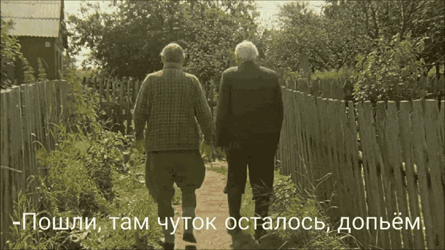 two older men walking down a path with a fence behind them