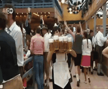 a woman carrying a tray of beer mugs in a crowd with a dw logo on the bottom right