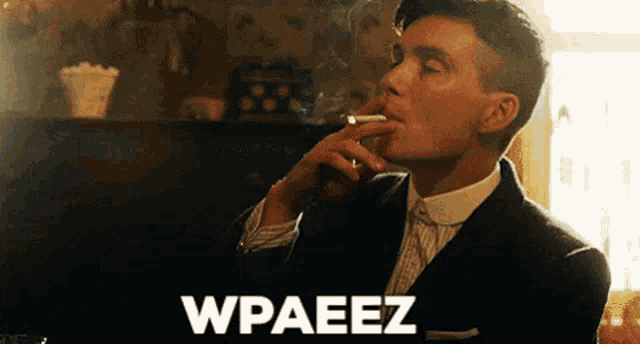 a man in a suit is smoking a cigarette and the word wpaeez is on the bottom right