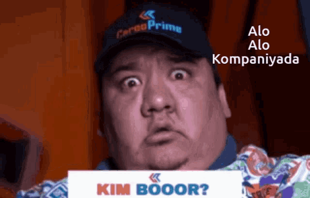 a man wearing a cargo prime hat holds up a sign that says kim booor