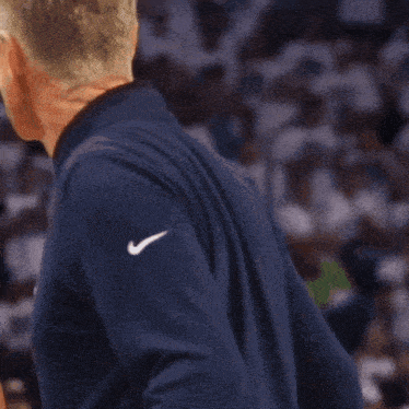 a man wearing a blue nike shirt stands in front of a crowd of people