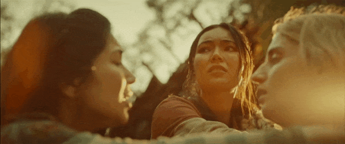 a group of three women are standing next to each other in a forest .