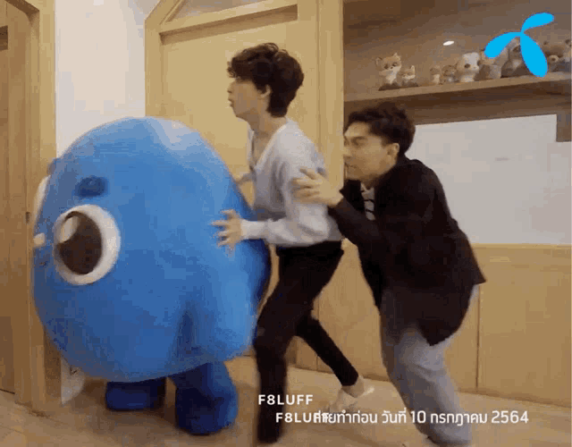 two men are playing with a blue stuffed animal that says fbluff on it