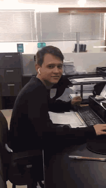a man wearing ear buds is sitting at a desk with a computer