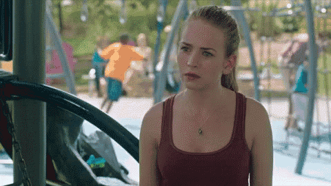 a woman in a red tank top is standing in front of a playground looking at something .