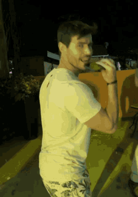 a man in a white t-shirt and floral shorts is standing in front of a yellow curb