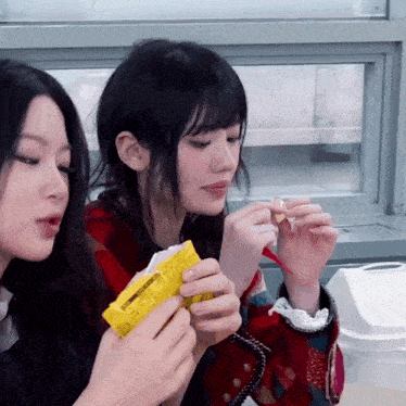 two girls are eating a snack together and one of them is holding a piece of paper that says ' korean ' on it