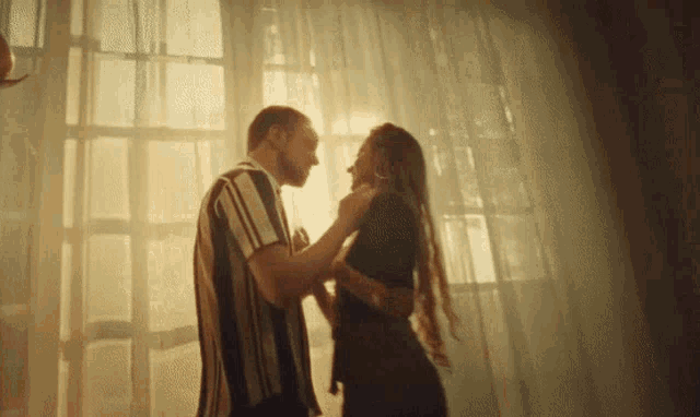 a man in a striped shirt is kissing a woman in front of a window