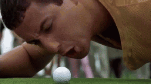 a man is laying on his stomach on a golf course looking at a golf ball .