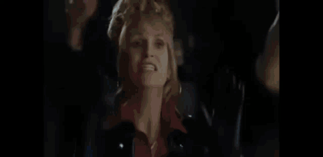 a woman in a red shirt is smiling in a dark room in a blurry photo .