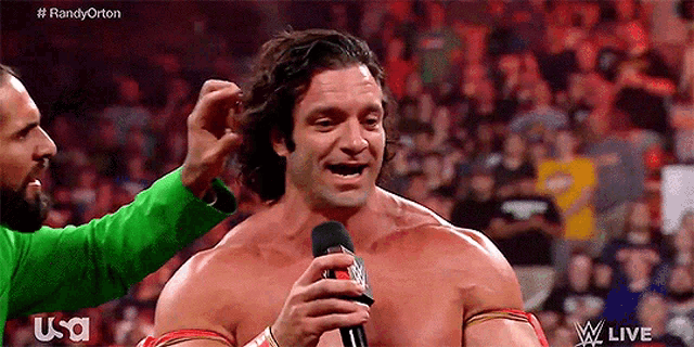 a man is talking into a microphone while another man holds his hair .