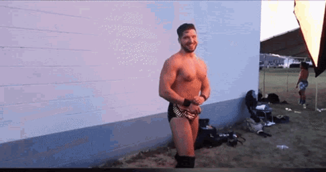 a shirtless wrestler standing in front of a white wall