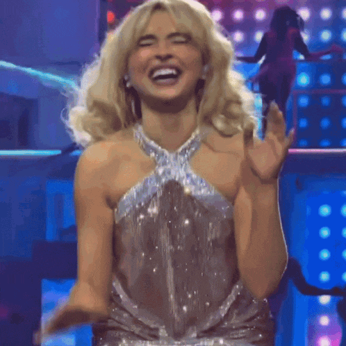 a blonde woman in a silver dress is laughing on stage