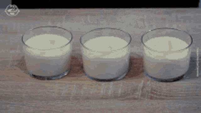 three glasses of yogurt are lined up on a wooden table