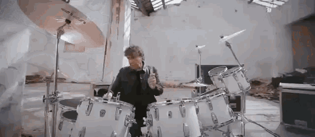 a man is playing drums in a room with a broken window .