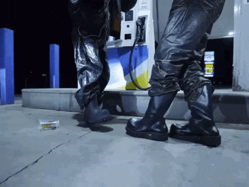 a person is standing in front of a gas pump with a cigarette on the ground in front of it