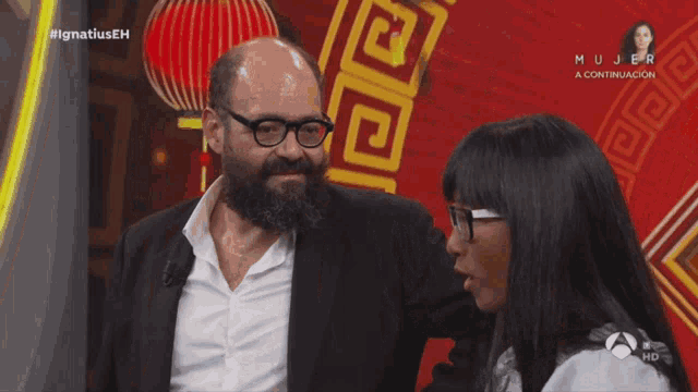 a man with a beard and glasses is talking to a woman on a television show