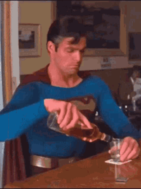 a man in a superman costume is pouring a bottle of whiskey into a glass