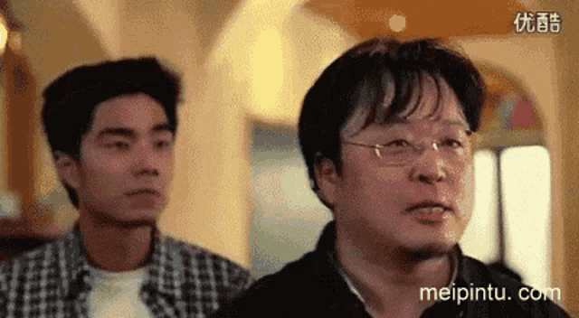 a man wearing glasses is standing next to another man in a room ..