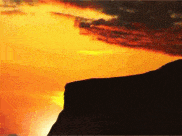 a sunset with a cliff in the foreground and a body of water in the background