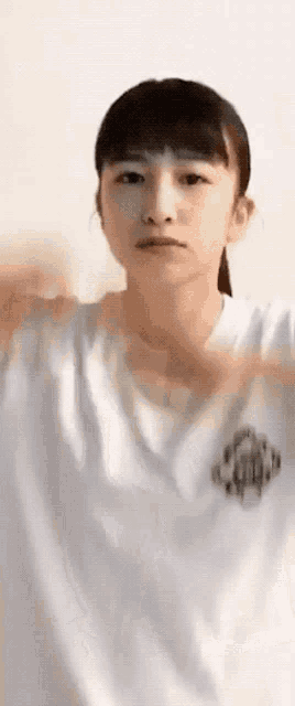 a young girl wearing a white t-shirt is making a heart shape with her hands .