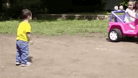 a boy in a yellow shirt is standing next to a pink toy jeep .