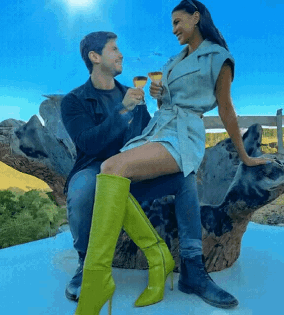 a man and a woman sitting on a tree trunk holding wine glasses