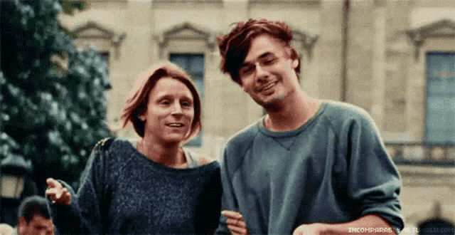 a man and a woman are standing next to each other and the woman is wearing a grey sweater