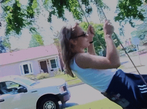 a woman in a white tank top is swinging on a rope
