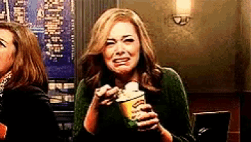 a woman in a green sweater is crying while holding a container of popcorn