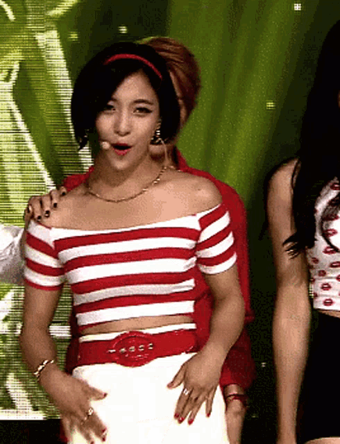 a woman in a red and white striped off the shoulder top stands on a stage
