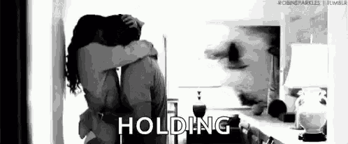 a black and white photo of a man and woman hugging each other in a room .