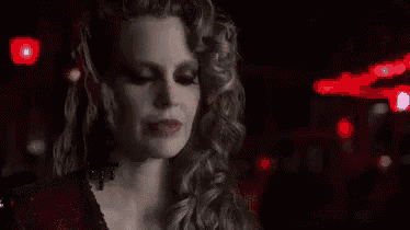 a woman in a red dress is looking at the camera in a dark room .