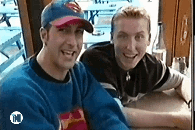 a man in a superman hat sits next to another man in a blue sweater