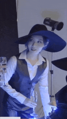 a woman wearing a hat and a vest is holding a glass of wine